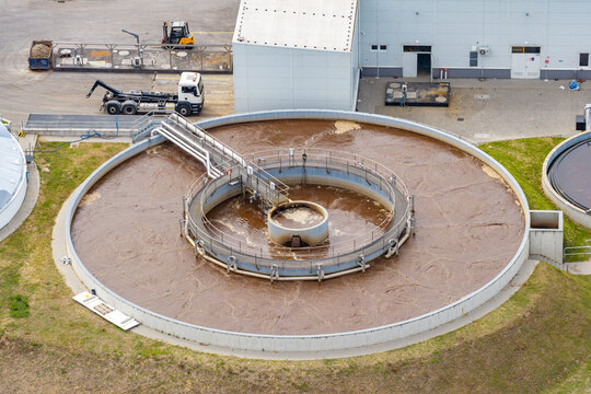 Aerial view of a circular aeration tank at a modern industrial wastewater treatment facility with concrete walls and piping in Poland.