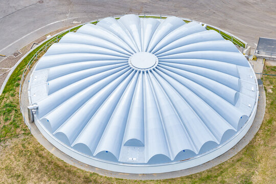 Aerial view of a large circular industrial tank with a distinctive ribbed roof structure at a modern processing facility in Poland.
