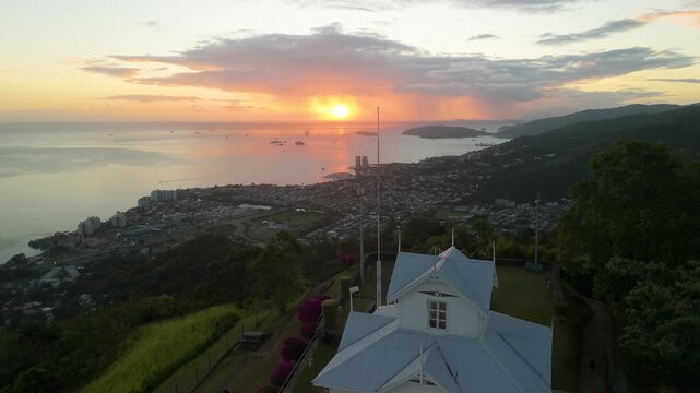 Aerial flyover from historic Fort George captures golden sunset panorama over Port of Spain coastline and mountains in Trinidad