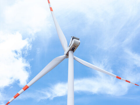 Aerial view of a wind turbine with white blades featuring red tips against a bright blue sky in Poland.