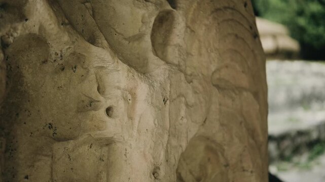 Detailed close-up shot of a weathered Maya stucco mask carving at Temple of the Great Jaguar, Tikal. Soft natural daylight highlights intricate ancient textures, jungle in background.