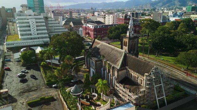 Gothic stone towers of Holy Trinity Cathedral rise above Port of Spain skyline in Trinidad surrounded by palm trees and city traffic