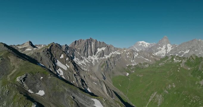 Drone rises above a rugged mountain ridge at the Great St Bernard Pass, revealing spectacular Alpine peaks beneath a crisp blue summer sky in the Swiss Alps.