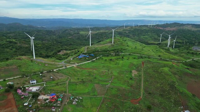 High altitude aerial view of wind turbines in Pililla, Rizal with rolling mountains, vegetation, and rural communities in the background.