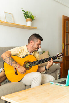 Man playing acoustic guitar learning from laptop at home