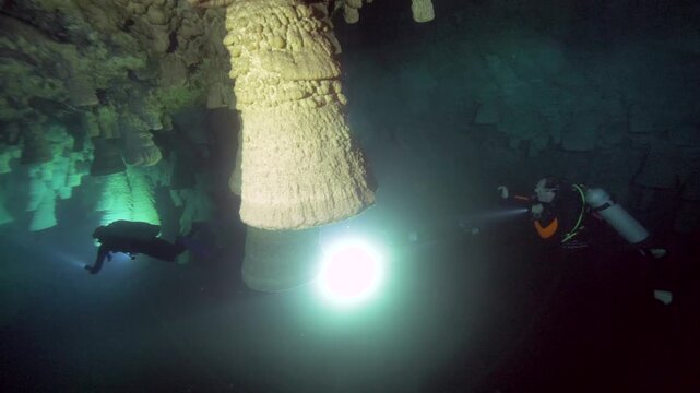 A diver carrying a bright lamp swims beside a massive pale formation inside Cenote Zapote, Quintana Roo, Mexico.
