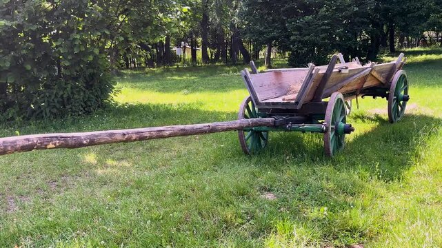 Old wooden horse cart with a long shaft standing in a green yard, traditional vintage agriculture concept