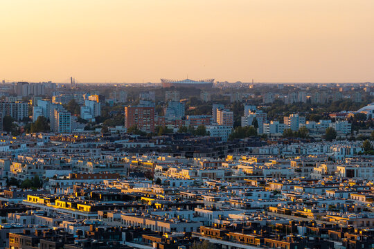 Aerial view of modern residential real estate and urban sprawl with the PGE Narodowy stadium in the distance during golden hour, Warszawa, Mazowieckie Voivodeship, Poland.