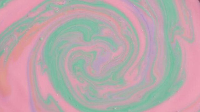 Swirling mixture of pink and green paint creates a mesmerizing spiral pattern in a shallow container, showcasing vibrant colors and fluid motion in artistic expression