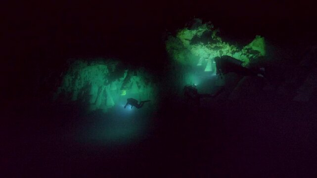 A narrow beam reveals a green-lit rock or mineral feature surrounded by darkness inside Cenote Zapote, Quintana Roo, Mexico.