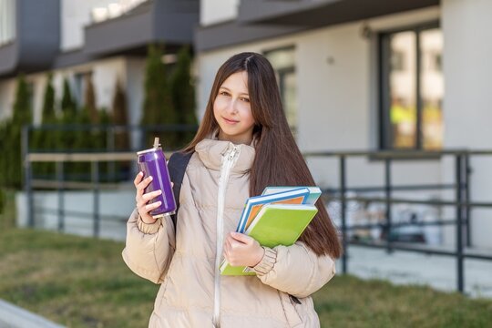 Teenage girl holding school notebooks and reusable water bottle outdoors before classes