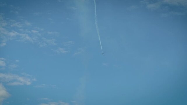 Airplane performing vertical dive with smoke trail in blue cloudy sky