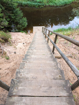 Wooden stairs descending down sandy slope to Valgejogi River pier in Nommeveski nature trail, Lahemaa National Park, Estonia.
