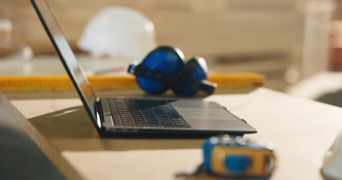 Laptop, carpentry and workshop with woodwork equipment, furniture manufacturing and design. Computer, empty workspace and tools on desk with safety earmuffs, ppe and industrial joinery production
