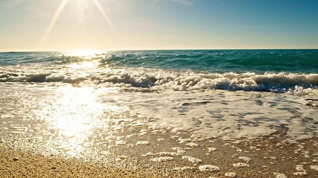 Ocean waves gently roll onto a sandy beach under a bright sun, creating a sparkling effect on the water surface and foamy white surf along the shore