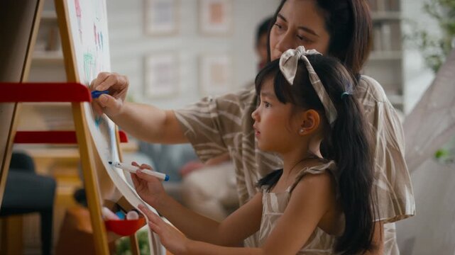 Asian mother or father teaching daughter doing homework on laptop at home. Parents supporting girl during summer break and back to school season.Concept of child education and family relationship life
