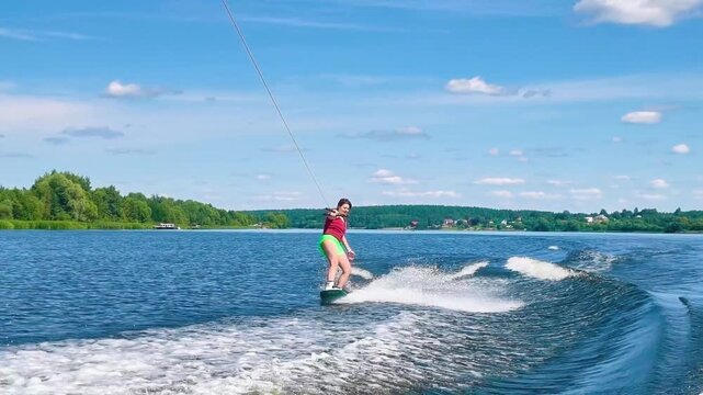 woman wakeboarder performing hand carve trick touching water surface while riding wave on river. concept of wakeboarding extreme water sport and active summer recreation