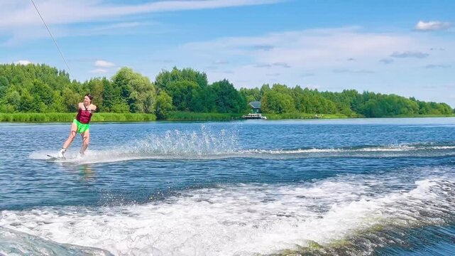 woman wakeboarding on wide river in sunny summer day. athletic female glides on water surface creating big splash. concept of wakeboarding extreme water sport and active summer recreation