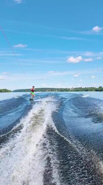 female wakeboarder riding on the crest of boat wake on wide river. athletic woman balances on board gliding over water waves. concept of wakeboarding extreme water sport and active summer recreation