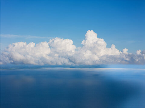 Aerial view of fluffy white cumulus clouds floating above the calm blue water of the lake under a clear sky in Jinotepe, Carazo, Nicaragua.