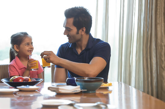 Father and daughter toasting with juice at dinning table