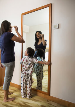 Woman applying make-up while her son look on