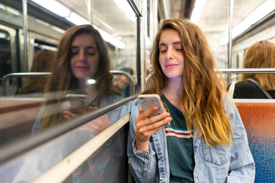 Smiling young woman in underground train looking at smartphone