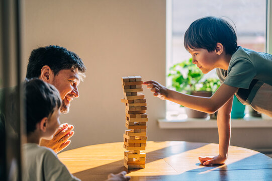 Father and son playing wooden block tower game indoors at home