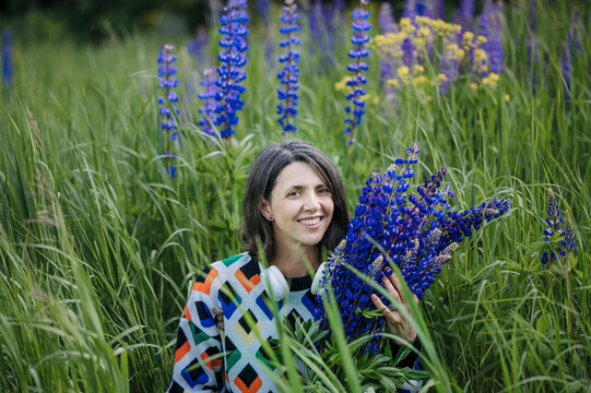 Smiling woman in sweater holds lupine flowers in a summer field