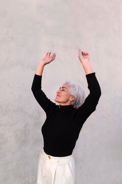 Carefree woman with eyes closed standing in front of wall