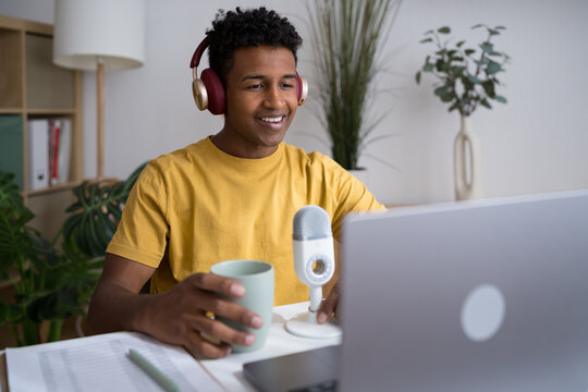 Smiling man recording podcast with coffee and headphones at home office