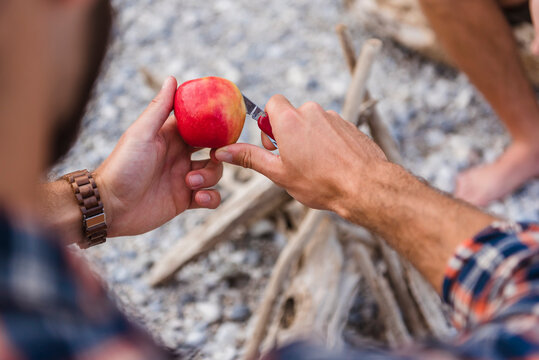 Man's hand cutting apple at camp fire