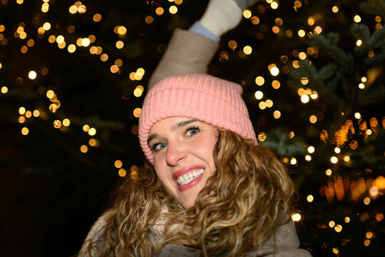 Smiling woman takes a selfie by a Christmas tree outdoors at night