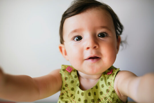 Portrait of baby girl stretching out her arms on white background