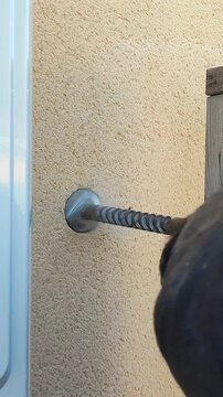 A worker drills a hole through an exterior wall to prepare the installation of an air conditioner in a residential building.