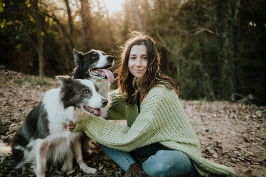 Woman sits outdoors in the autumn forest with her dogs