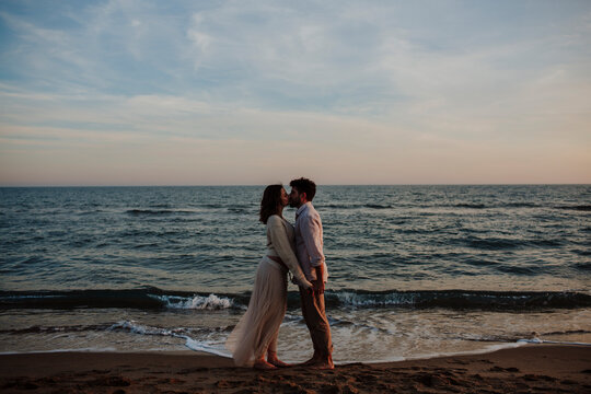 Pregnant woman and man kissing on the beach at sunset