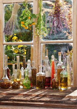 Bottles of infused oil and drying herbs on a rustic windowsill