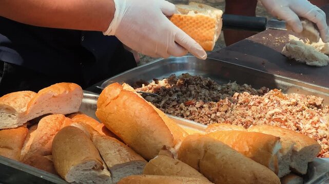 Street food vendor preparing kokorec sandwich on a grill at an outdoor market. Traditional Turkish fast food made from seasoned lamb intestines served in fresh bread. High quality 4k footage