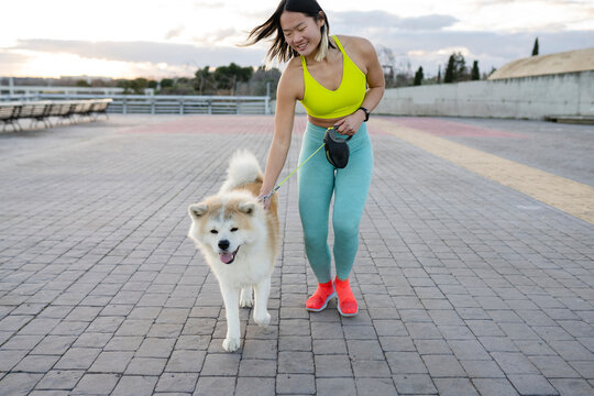 Smiling sportswoman dog walking on footpath