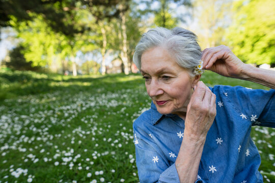 Smiling retiree putting a daisy behind the ear in a sunny park