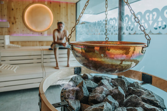 Container hanging over coal while mature man in background at finnish sauna