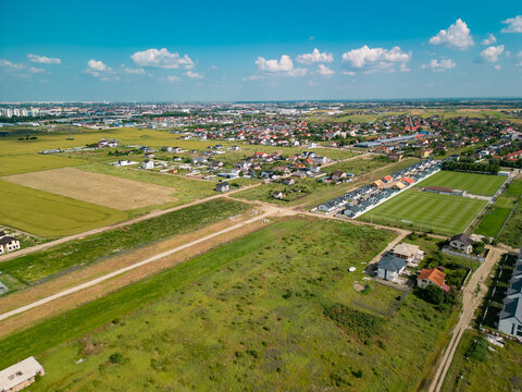 High angle drone shot showing vibrant residential neighborhood with suburban houses, red roofs, green trees, and blue sunny sky in Domnesti, Ilfov, Romania.