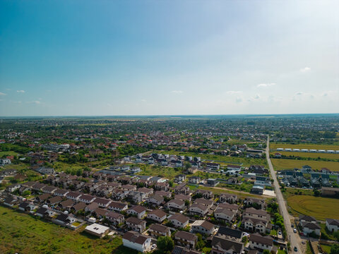 High angle drone shot showing vibrant residential neighborhood with suburban houses, red roofs, green trees, and blue sunny sky in Domnesti, Ilfov, Romania.
