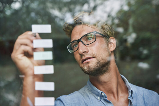 Casual young businessman with adhesive notes behind windowpane in office