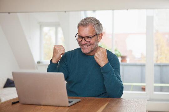 Mature man at home looking at laptop cheering