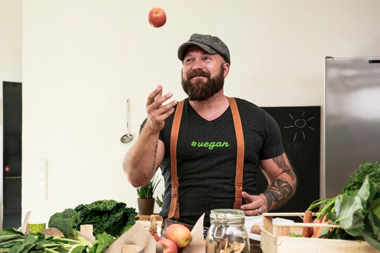 Vegan man juggling with apples in his kitchen