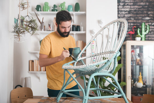 Bearded man painting wicker armchair at home