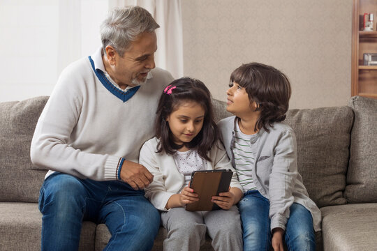 Happy grandfather sitting with grandchildren using digital tablet