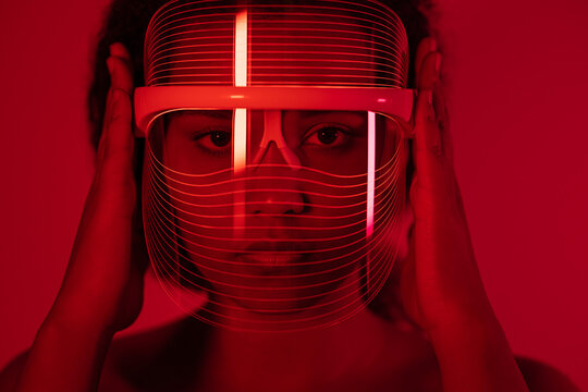 Close-up of woman wearing red light therapy mask against wall at home